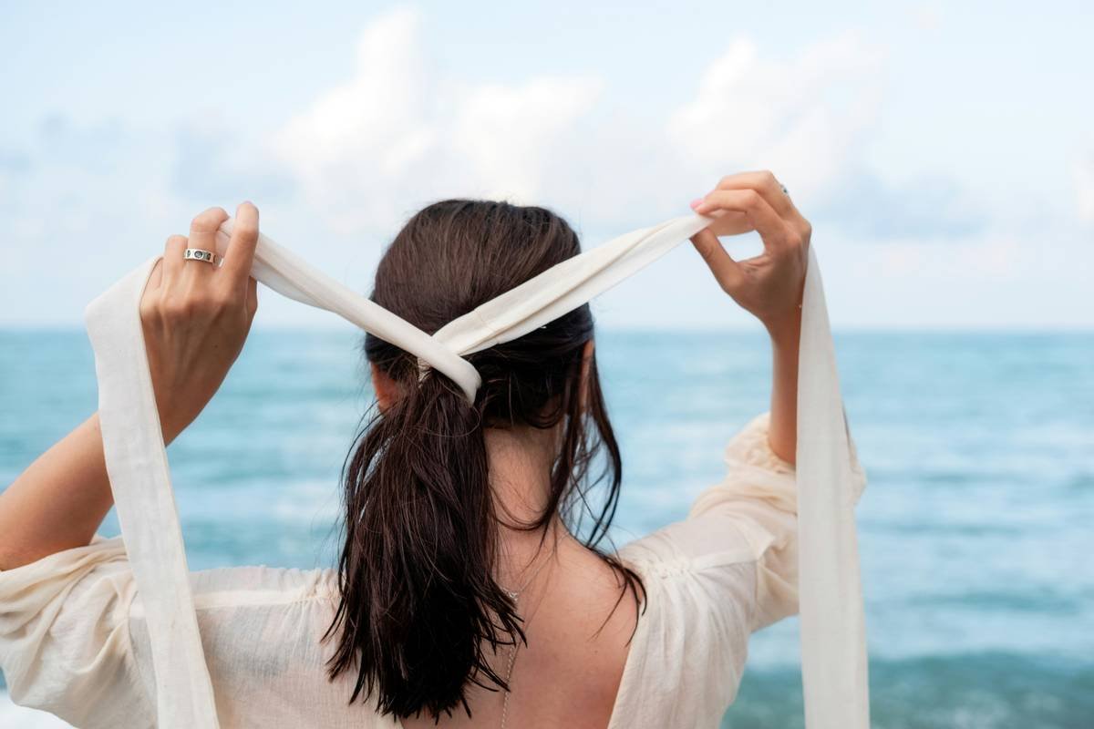 Woman styling her hair with a silk fashion hair tie while wearing a printed hair scarf
